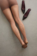Overhead view of legs in the Back Vine Sheer Tights in Coffee, lying on the floor next to a pair of heels, showing the vine pattern.