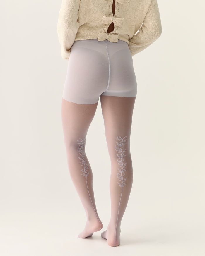 Person wearing sheer tights with a back vine floral embroidery in lilac and natural smoothing panty.