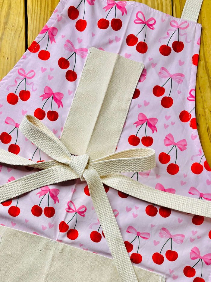 amanda bright designs close-up of a light pink apron with a repeating cherry and bow pattern motif