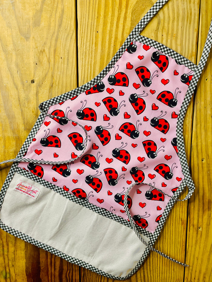 Amanda Bright Designs Children's ladybug hearts apron pink with red and black ladybugs and black checkered trim