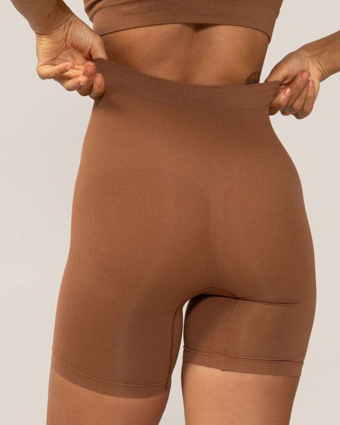 Brown shapewear being worn against a neutral background