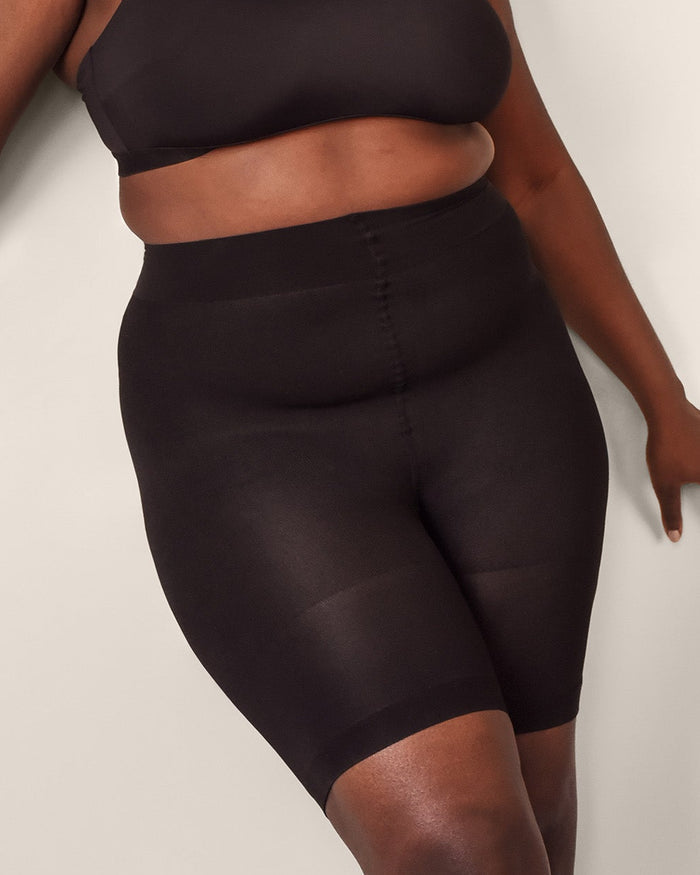 A person wearing black shaping undershorts and a matching sports bra, standing against a plain background.