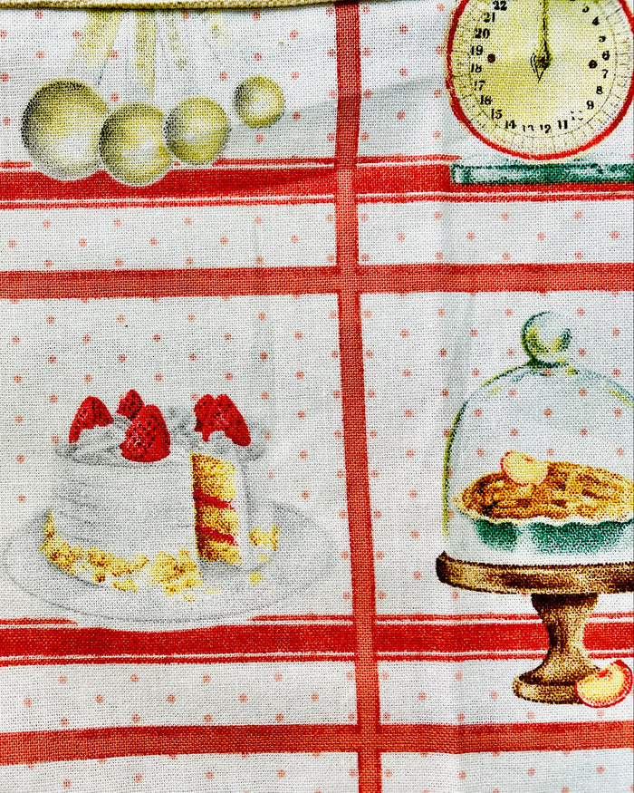 Amanda Bright Designs white baking apron with a red checkered pattern featuring illustrations of baking-related items like a cake, pie, and rolling pin domed cupcakes with canvas pockets and cotton strings