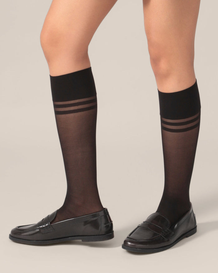 Black knee-high socks with thin stripes worn by a person on a plain background