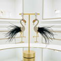 Flamingo-shaped earrings with black feathers on a gold stand against a light background