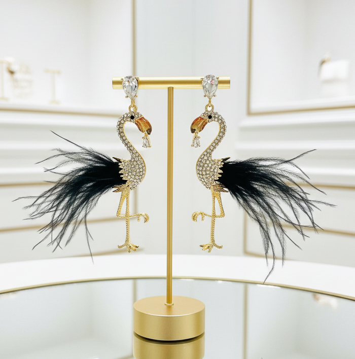 Flamingo-shaped earrings with black feathers on a gold stand against a light background