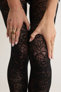 Hands adjusting the Floral Lace tights in Black at the thigh, showing the delicate lace pattern up close.