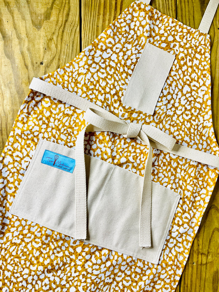 Apron with a leopard print pattern in shades of yellow, brown, and white, featuring a front pocket and an adjustable neck strap.