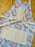 Amanda Bright Designs Howdy Cherry Cowgirl Apron featuring state of texas in cake form with words yeehaw and howdy in icing with cherries on baby blue background