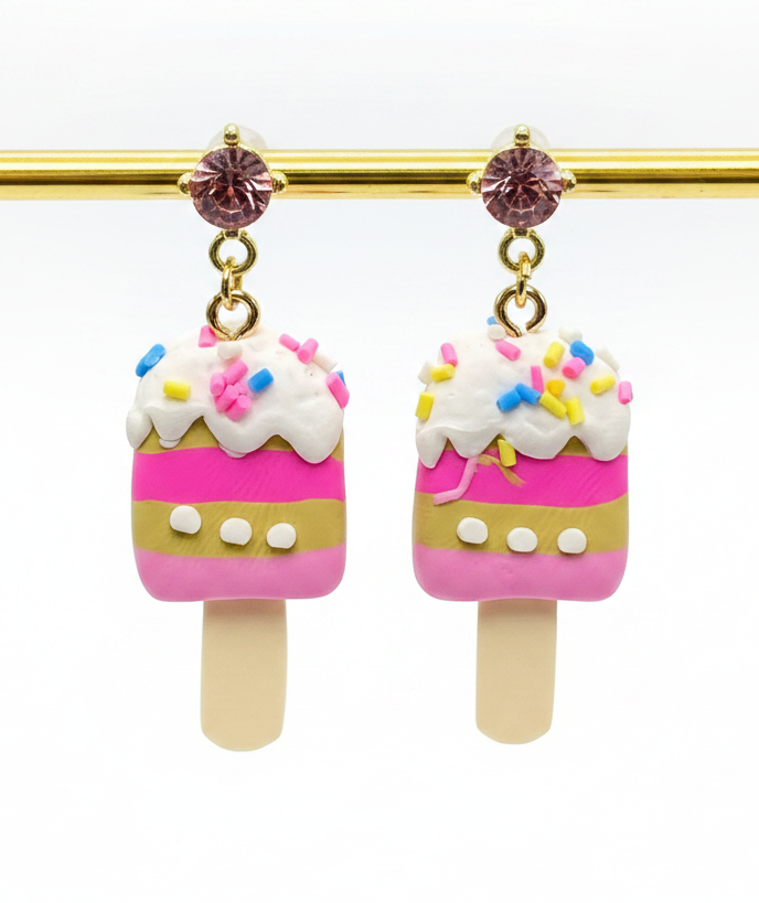 Ice cream pop-shaped earrings with pink and white design on a gold stick against a white background.