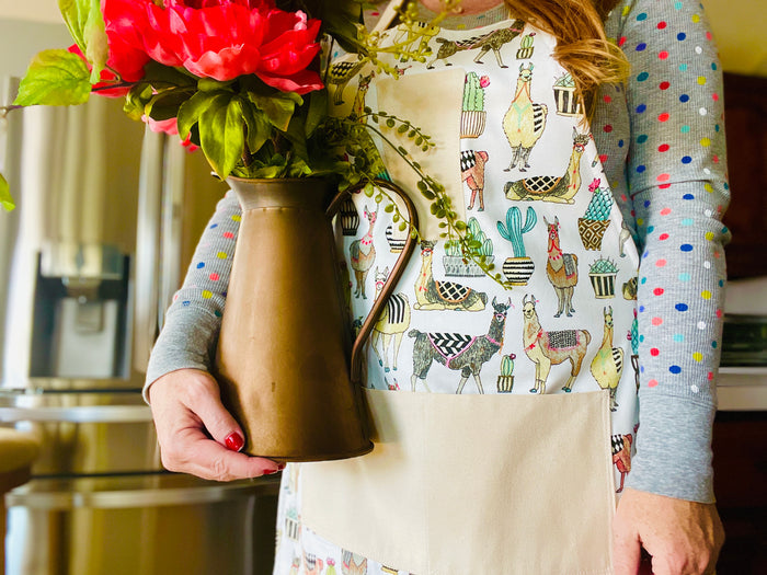 amanda bright designs isabella llama flowering cactus southwest theme apron on model in kitchen holding copper pitcher wtih flowers