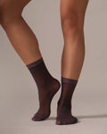 Purple plum socks with polka dots worn by a person on a beige background