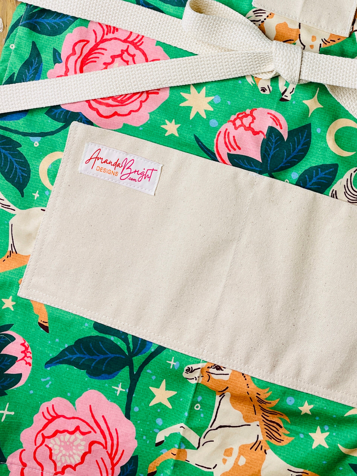 moonlit meadows pockets apron Galloping pintos, blooming peonies, and celestial moons and stars come together on a vibrant emerald green background