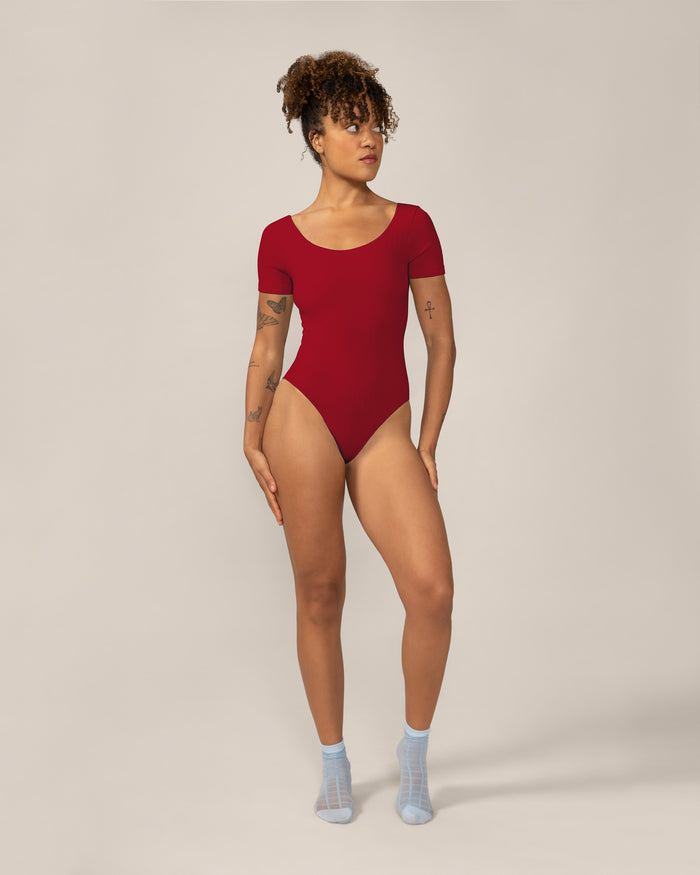 Woman wearing a red bodysuit on a plain background