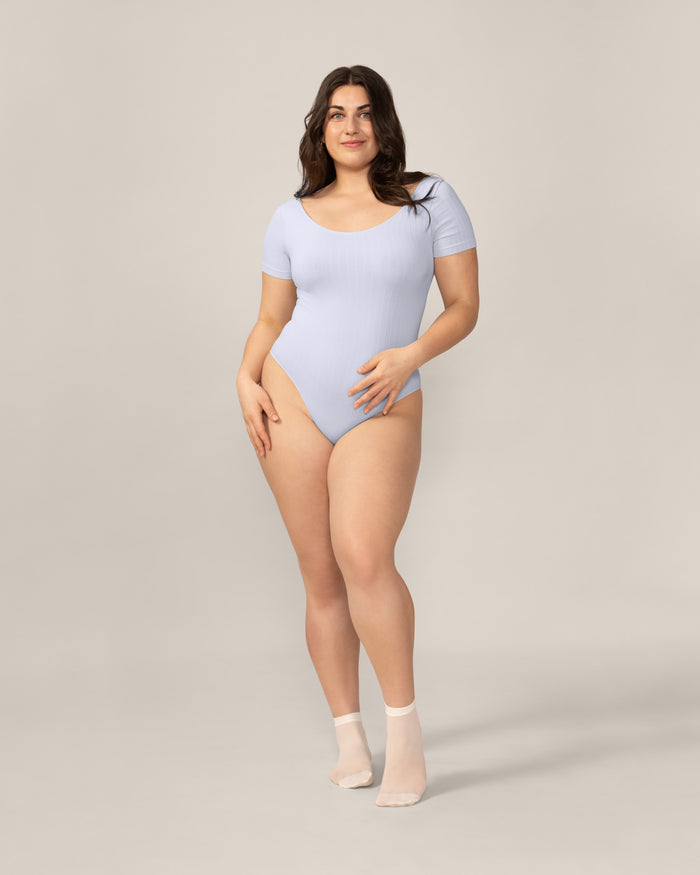 Woman wearing a light blue bodysuit against a plain background