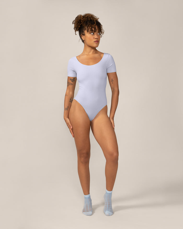 Woman wearing a light blue bodysuit on a beige background