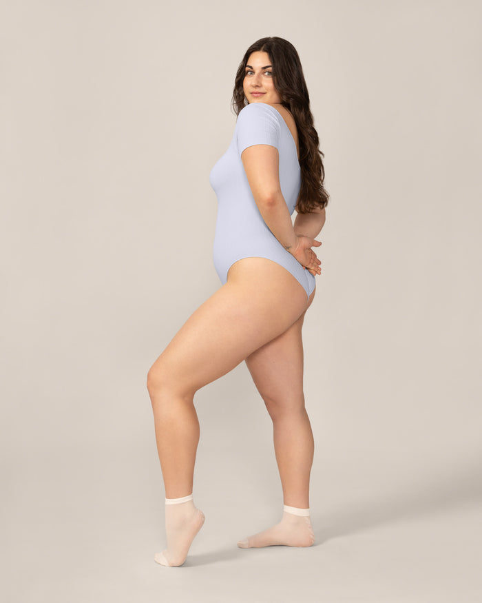 Woman wearing a light blue bodysuit on a neutral background