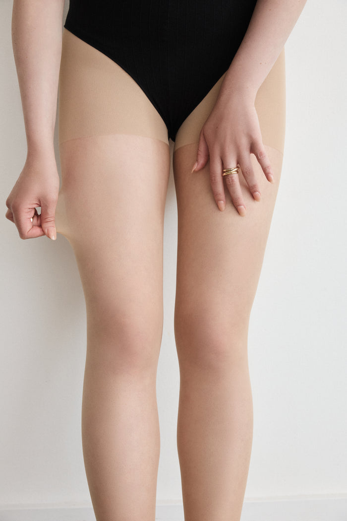 Close-up of a hand at the hip, showing the Shaping Panty waistband under black underwear on the Sheer Shaping Tights 30D in Dune.