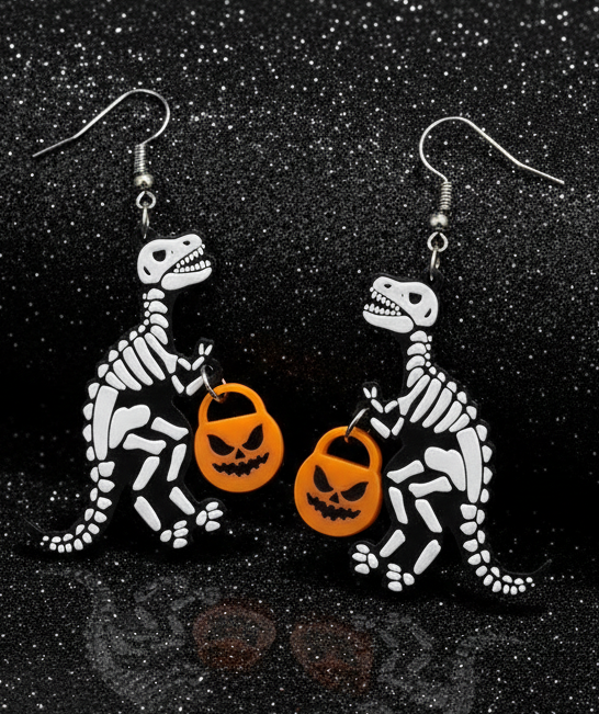 Dinosaur skeleton earrings holding Halloween pumpkins on a black background