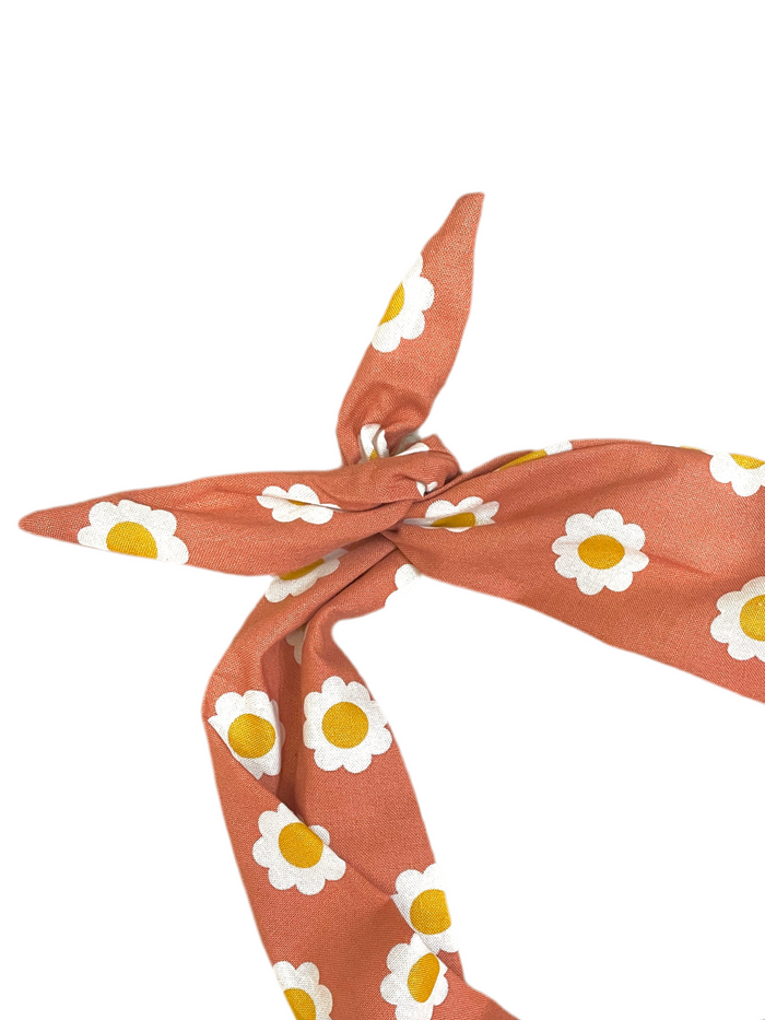 Amanda Bright Designs terracotta orange moldable cotton tie headband with a white and yellow daisy pattern, tied in a knot against a solid white background.
