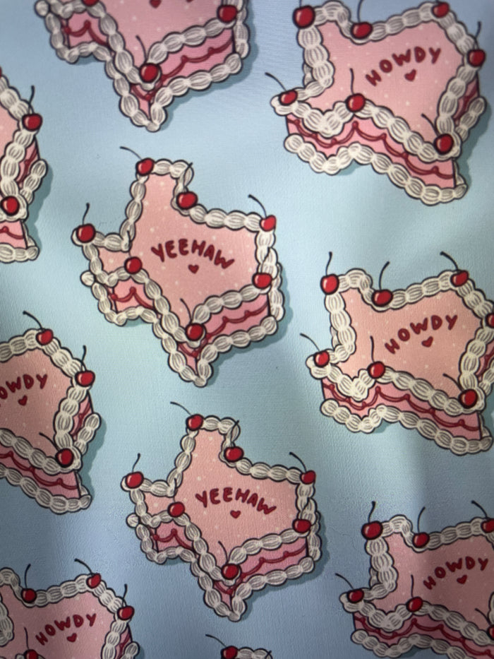 Pink Texas Shaped Iced Cakes with frosting and cherries on a light blue backgroun Amanda Bright Designs Couture Apron Collection