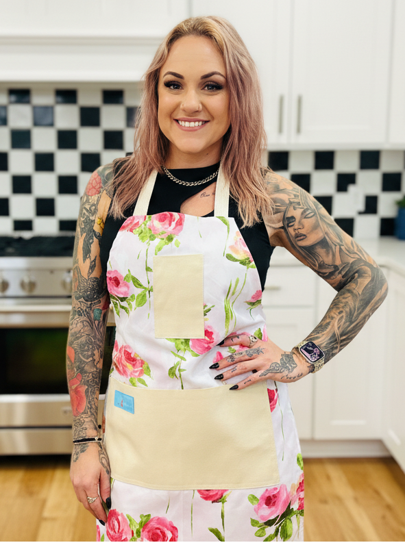 Woman wearing Amanda Bright Designs Vivien floral apron in a kitchen with white cabinets and black and white checkered tiles.