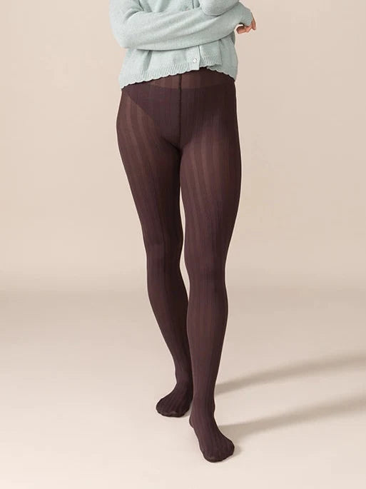 Woman wearing a light blue sweater and dark brown tights against a beige background